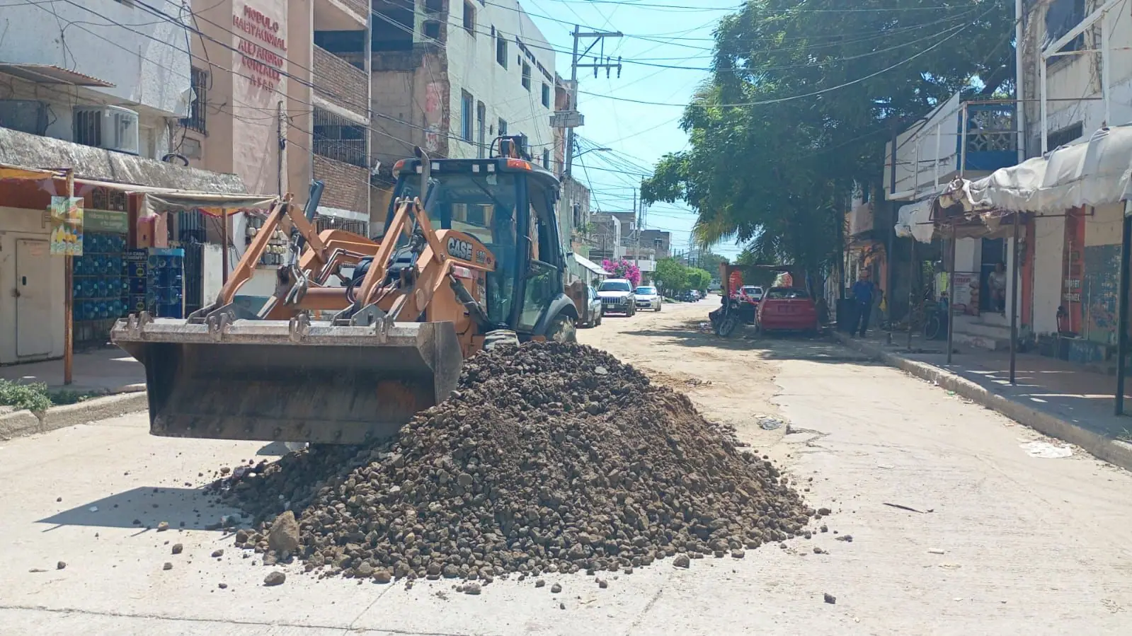 Retroexcavadora Case con el cargador frontal junto a un montón de material en la calle